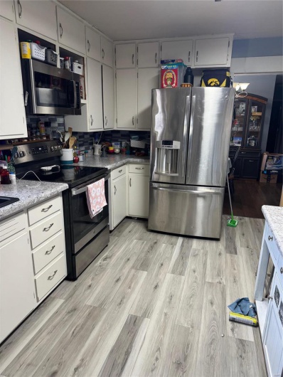 Kitchen with refrigerator, light wood-type flooring, stove, white cabinets, and decorative backsplash