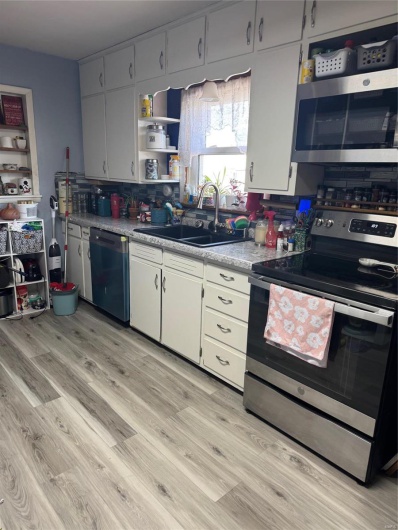 Kitchen featuring stove, dishwasher, light wood-type flooring, sink, and white cabinetry