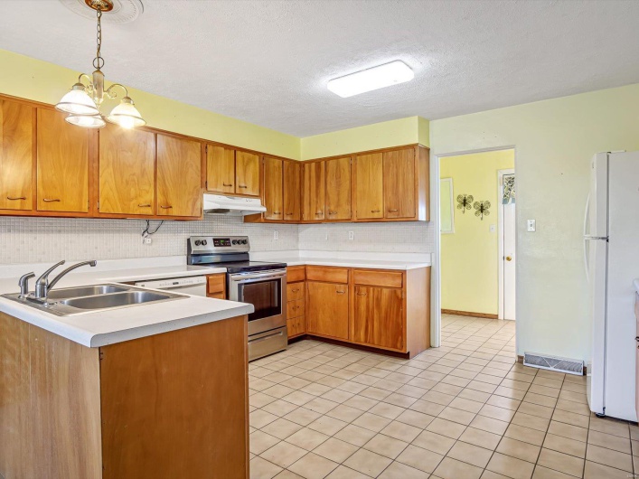 Kitchen featuring electric range, freestanding refrigerator, light countertops, under cabinet range hood, and a sink