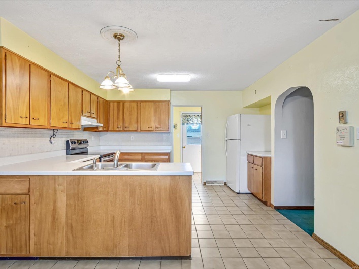 Kitchen featuring light countertops, a sink, a peninsula, stainless steel range with electric stovetop, and under cabinet range hood