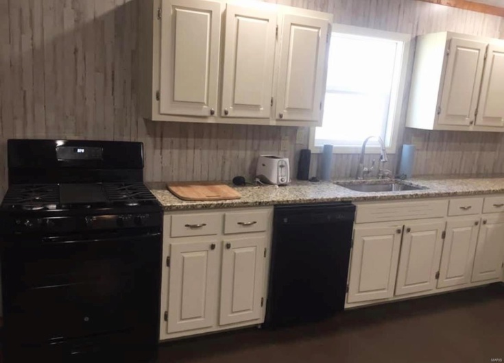 Kitchen with black appliances, white cabinetry, backsplash, and a sink
