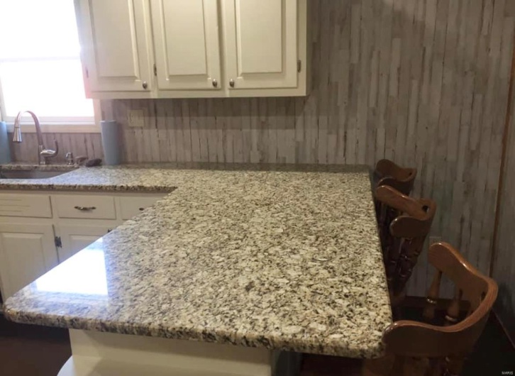 Kitchen featuring light stone counters, white cabinetry, and a sink