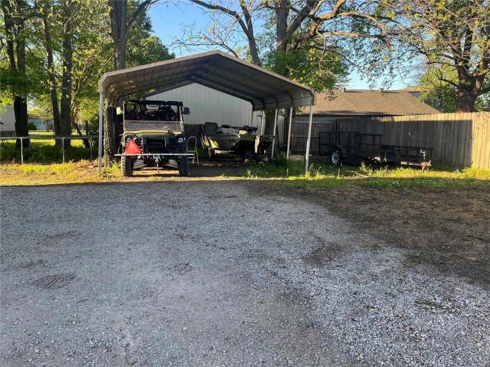 View of parking with driveway, fence, and a carport