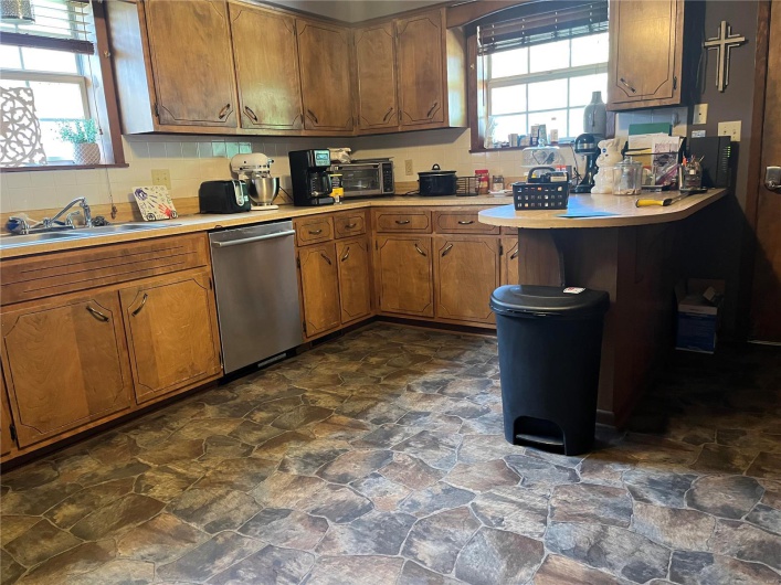 Kitchen featuring brown cabinetry, light countertops, dishwasher, and a sink