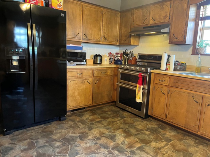 Kitchen with brown cabinets, light countertops, backsplash, appliances with stainless steel finishes, and under cabinet range hood