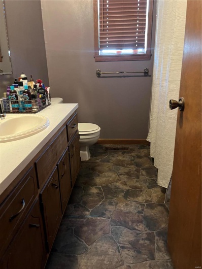 Full bath featuring toilet, baseboards, stone finish floor, and vanity
