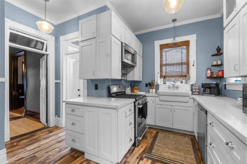 Kitchen with pendant lighting, white cabinetry, sink, wood look tile flooring, and stainless steel appliances