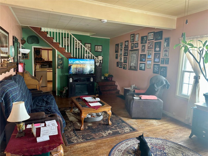 Living area featuring stairs, baseboards, wood finished floors, and crown molding