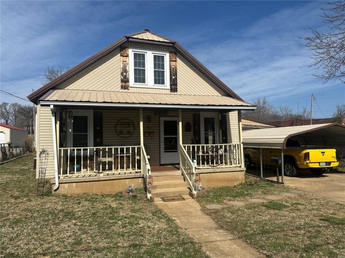 Bungalow-style home with metal roof, covered porch, a detached carport, and a front yard