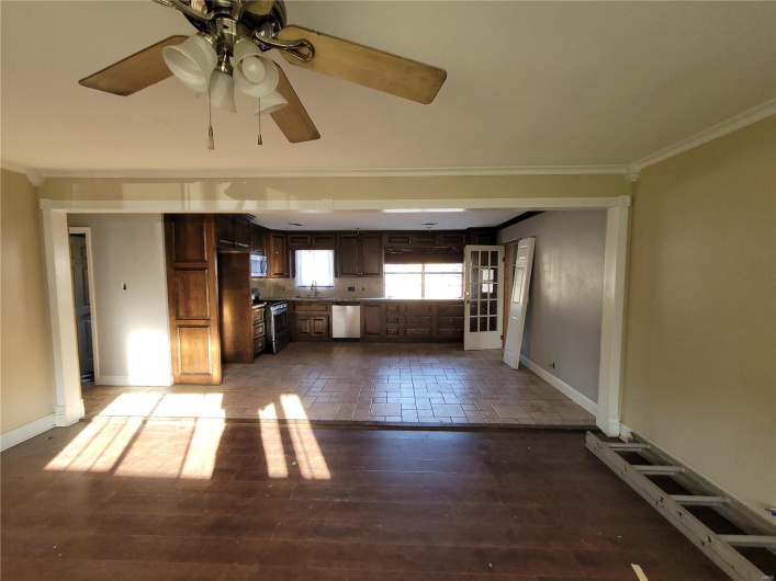 Unfurnished living room featuring a sink, wood finished floors, a ceiling fan, baseboards, and ornamental molding
