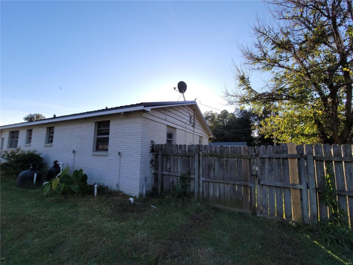 View of property exterior featuring fence, a lawn, and brick siding