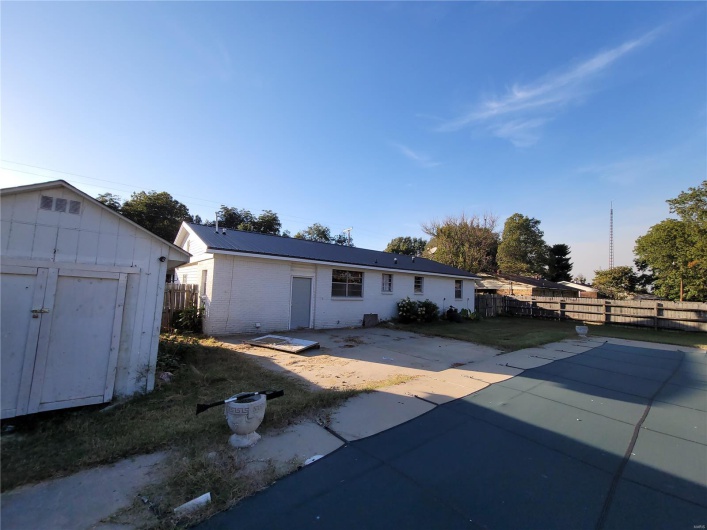 Ranch-style home featuring metal roof, an outdoor structure, fence, a storage unit, and a patio area