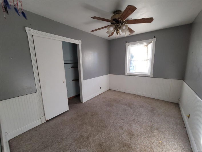 Unfurnished bedroom with a ceiling fan, a closet, a wainscoted wall, and light carpet