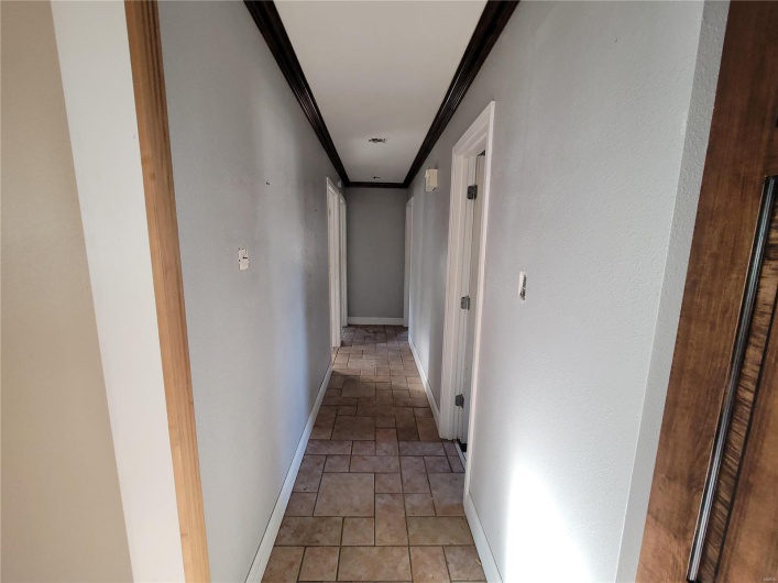 Hall featuring ornamental molding, baseboards, and stone tile floors