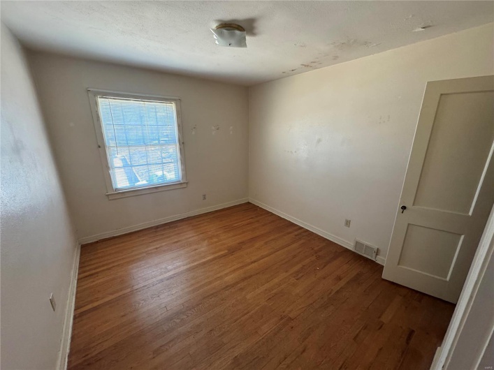 Empty room featuring visible vents, a textured ceiling, baseboards, and wood finished floors