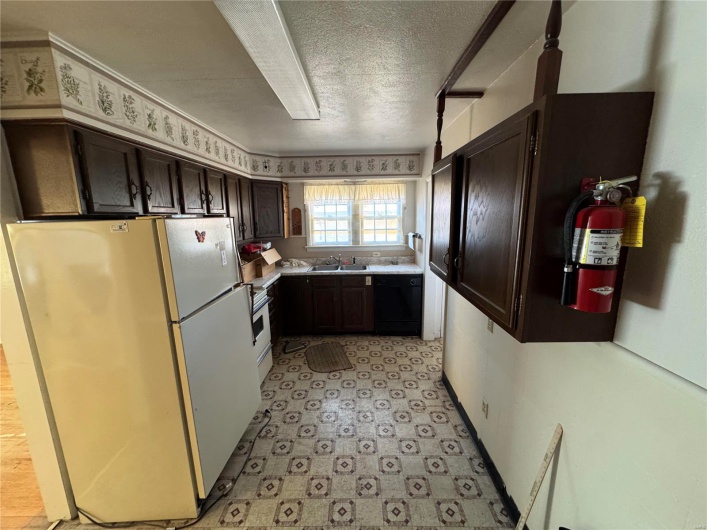 Kitchen with dark brown cabinetry, a sink, light countertops, freestanding refrigerator, and dishwasher