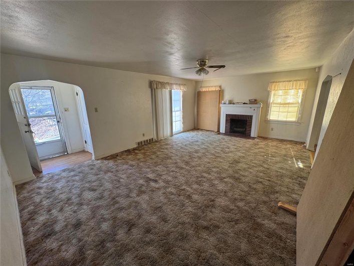 Unfurnished living room featuring arched walkways, carpet floors, visible vents, a ceiling fan, and a brick fireplace