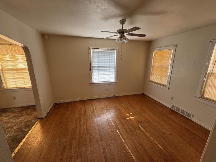 Empty room featuring arched walkways, dark wood-type flooring, a ceiling fan, visible vents, and baseboards