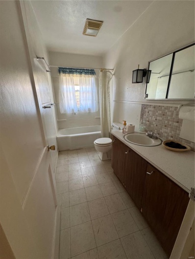 Full bath with shower / tub combo with curtain, backsplash, toilet, vanity, and tile patterned floors
