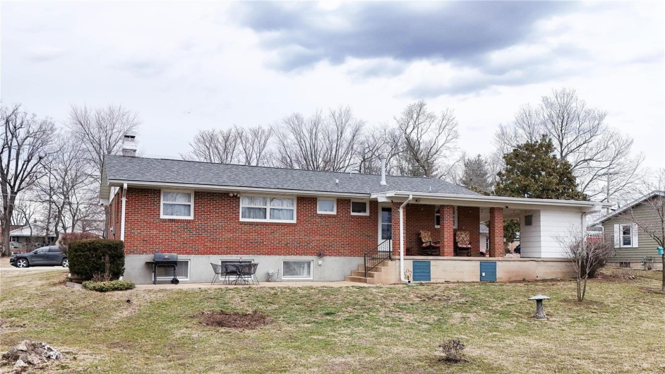 View of front of property featuring brick siding, a chimney, a shingled roof, a porch, and a front lawn