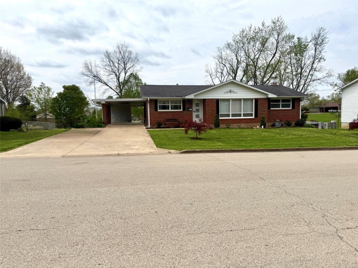 View of front of home with brick siding, a front yard, a chimney, concrete driveway, and a carport