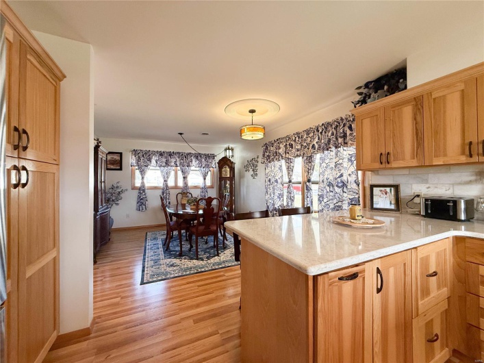 Kitchen with light stone counters, a toaster, a peninsula, backsplash, and light wood finished floors