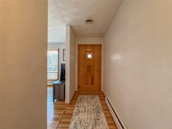 Doorway to outside with a baseboard heating unit, a textured wall, light wood finished floors, and visible vents