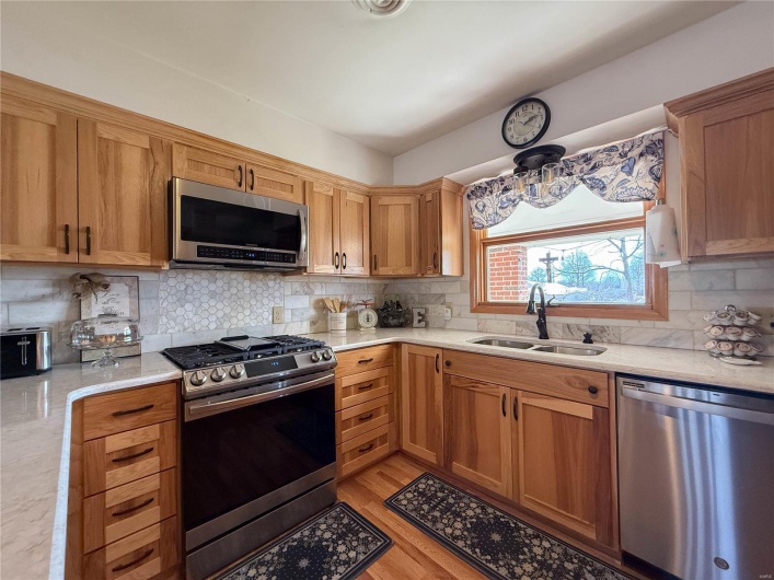 Kitchen with appliances with stainless steel finishes, light wood-type flooring, a sink, and decorative backsplash
