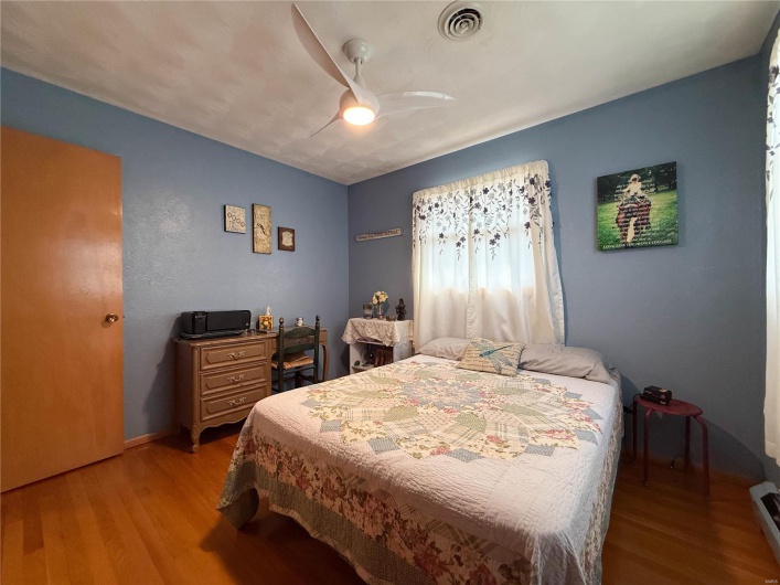 Bedroom with baseboard heating, wood finished floors, visible vents, and a ceiling fan