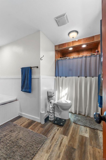 Full bathroom with visible vents, a shower with shower curtain, toilet, wainscoting, and wood finished floors