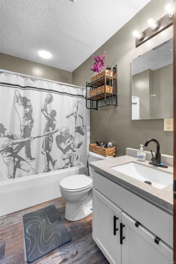 Bathroom featuring a textured ceiling, toilet, wood finished floors, vanity, and shower / bath combination with curtain