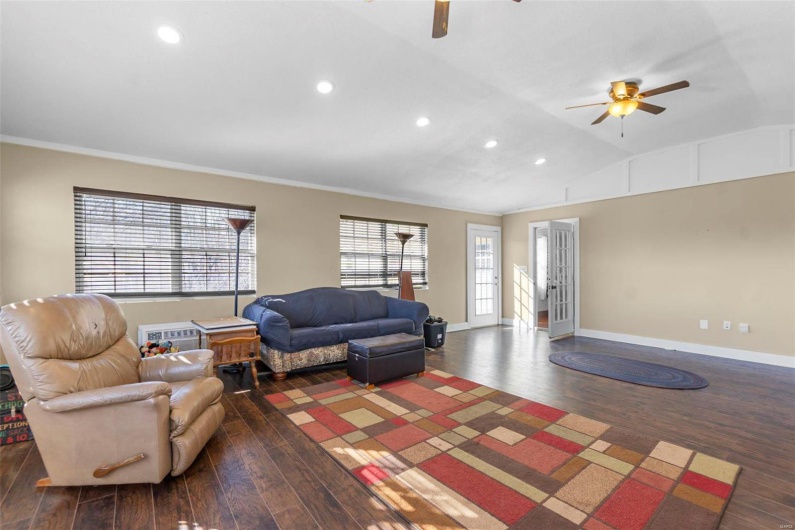 Living area with lofted ceiling, dark wood-style flooring, ceiling fan, and baseboards