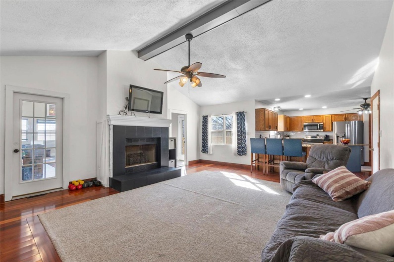 Living area with a tile fireplace, dark wood-style flooring, lofted ceiling with beams, and a textured ceiling