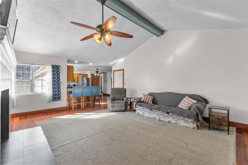 Living room featuring vaulted ceiling with beams, a ceiling fan, a textured ceiling, wood finished floors, and baseboards