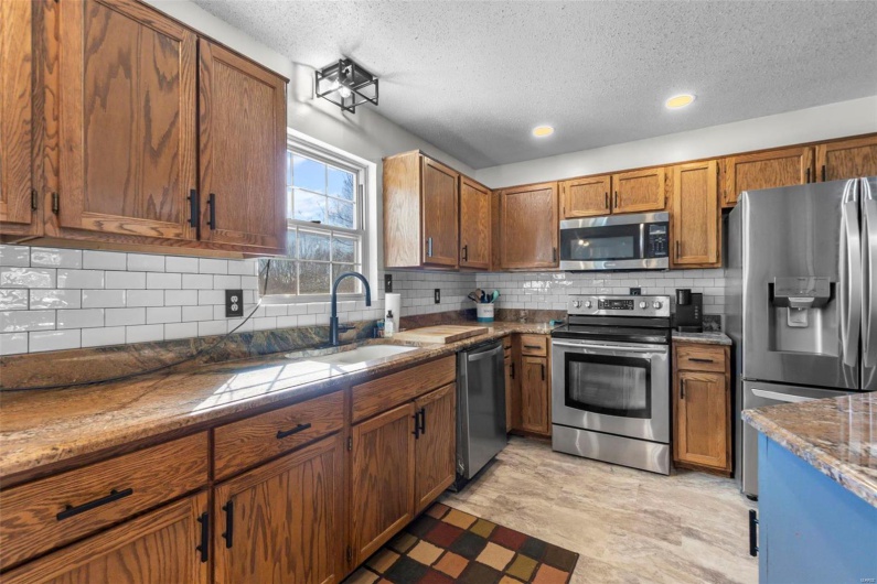 Kitchen featuring a textured ceiling, a sink, appliances with stainless steel finishes, backsplash, and brown cabinets