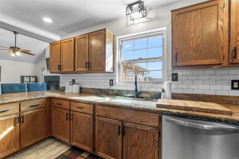 Kitchen featuring lofted ceiling, a sink, stainless steel dishwasher, backsplash, and brown cabinets