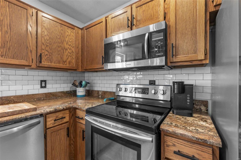 Kitchen featuring dark stone counters, stainless steel appliances, and brown cabinetry