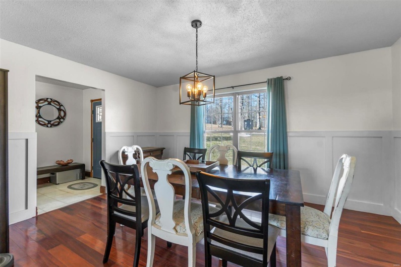 Dining space with an inviting chandelier, a textured ceiling, wood finished floors, and a wainscoted wall