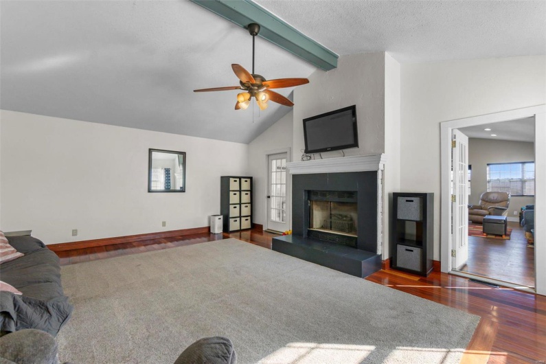 Living area with baseboards, dark wood-type flooring, a tiled fireplace, and beamed ceiling