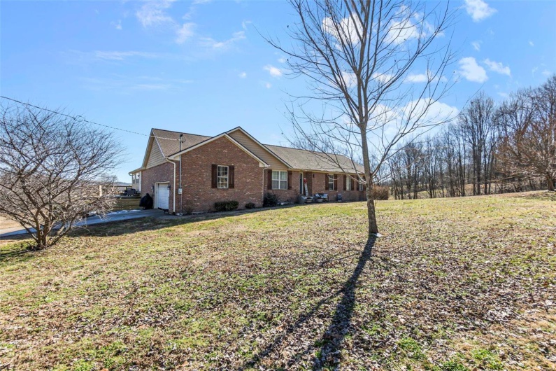 View of side of home with a garage, a yard, brick siding, and concrete driveway