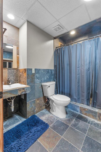 Bathroom with tile walls, a paneled ceiling, stone tile flooring, visible vents, and toilet