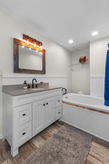 Full bathroom with recessed lighting, vanity, a bath, and wood finished floors