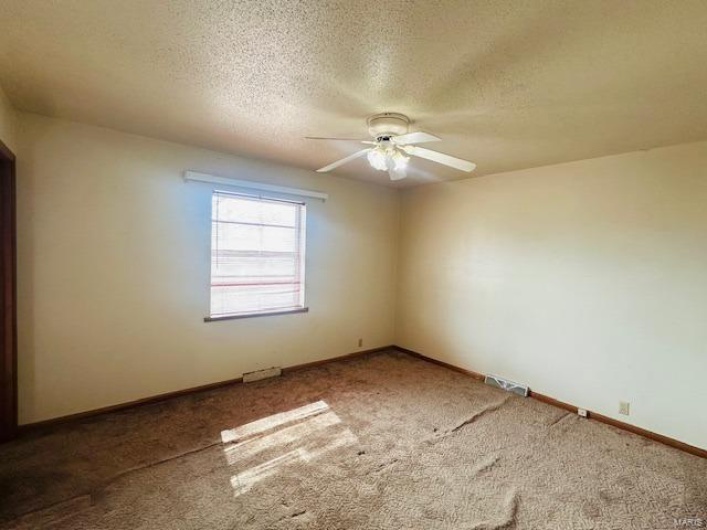 Carpeted spare room featuring a ceiling fan, a textured ceiling, and baseboards