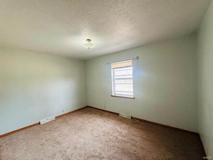 Unfurnished room featuring carpet, a textured ceiling, visible vents, and baseboards