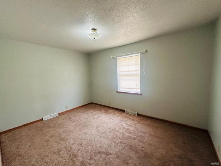 Carpeted empty room featuring a textured ceiling, visible vents, and baseboards