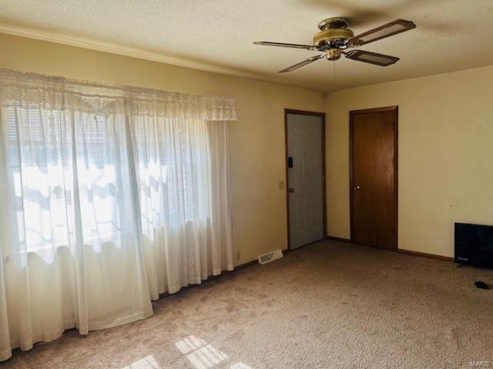 Spare room with a textured ceiling, light carpet, visible vents, and a ceiling fan