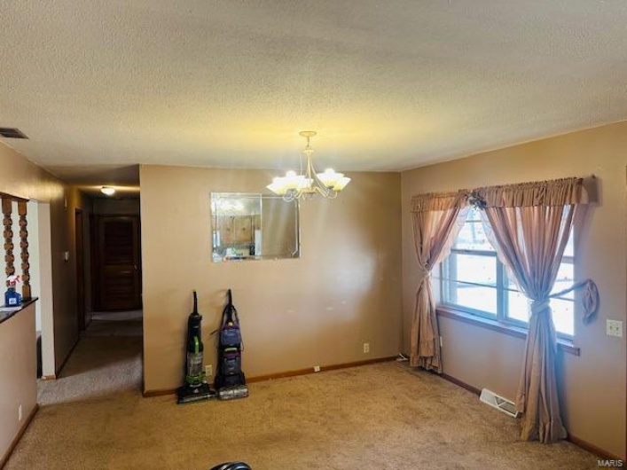 Unfurnished dining area with a textured ceiling, carpet flooring, visible vents, and an inviting chandelier