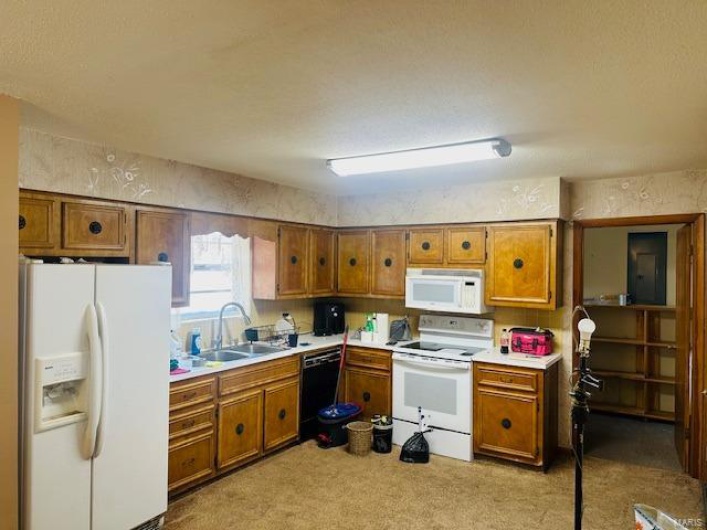 Kitchen with brown cabinetry, white appliances, light countertops, and a sink