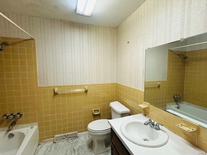 Full bathroom with wallpapered walls, visible vents, a wainscoted wall, a textured ceiling, and washtub / shower combination
