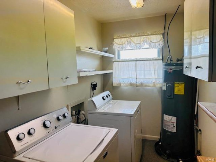 Laundry room featuring water heater, washer and clothes dryer, a textured ceiling, and cabinet space